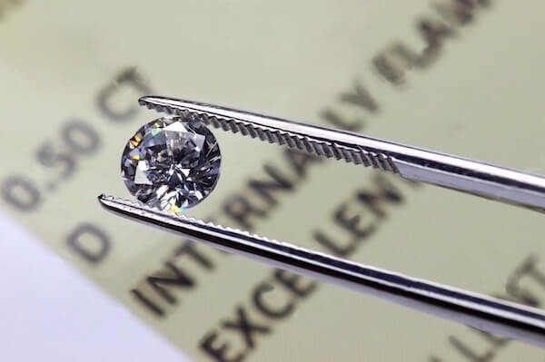 Diamant in Pinzette über Diamantenzertifikat Pinzette hält einen Diamanten zwischen ihren Zangen über einem Diamantenzertifikat - Diamantenzertifikate
